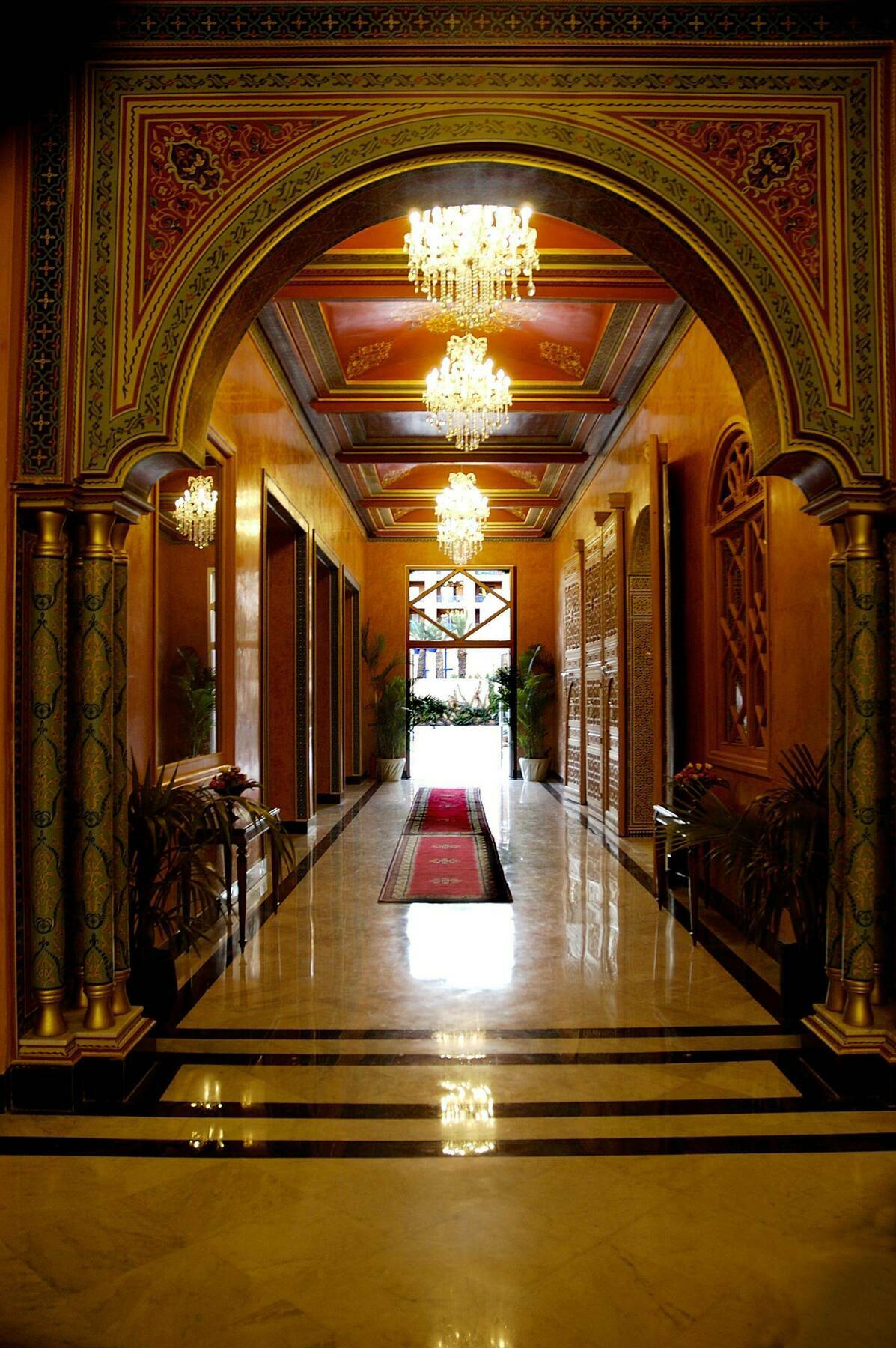 大莫加多尔梅纳拉酒店 马拉喀什 内观 照片 The photo depicts a luxurious corridor with an ornate, opulent design. The walls are painted in warm tones, and the ceiling features intricate patterns. Bright chandeliers hang from the ceiling, providing soft lighting. The floor is made of polished 
